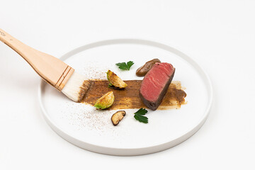 On a white background, plating meat and vegetables on a plate and pouring sauce with a ladle
