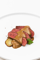 On a white background, sauce being drizzled over meat and vegetables on a plate
