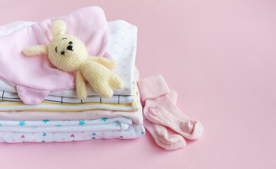 Baby knitted toy of bunny next to a stack rompers for kids