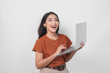 Smiling young woman wearing brown shirt holding laptop with a happy expression isolated over white background.