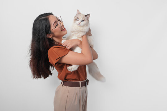Portrait of young Asian woman in brown shirt holding her ragdoll cat and smiling to the camera isolated over white background.