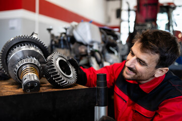 Experienced mechanic or serviceman holding gears parts inside workshop.