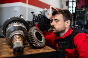 Nervous mechanic having problems at work in workshop. Spare parts, gears and tools around him.