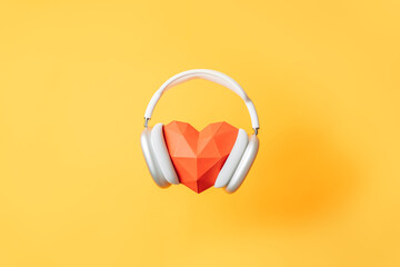White wireless headphones on a large red origami heart against a yellow background.