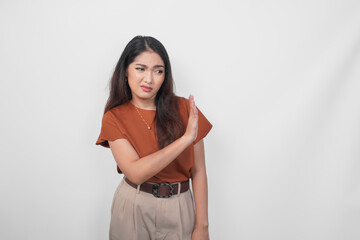 Upset young Asian woman wearing brown shirt doing stop sign with palm of the hand over white...