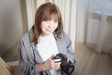 Senior old elderly woman with black camera with a large lens indoors in the studio. A professional photographer. Age Hobby