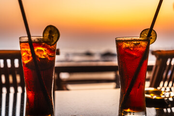 Negroni Cocktail in crystal glass with ice cubes and orange slices with blurred sea beach in...