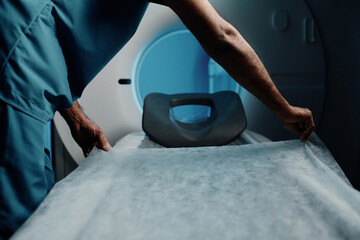 Unrecognizable male radiographer preparing CT scanner bed covering it with disposable sheet at work in modern hospital - obrazy, fototapety, plakaty