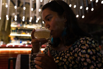 Smiling confident young Indian woman drinking cocktail in a nightclub
