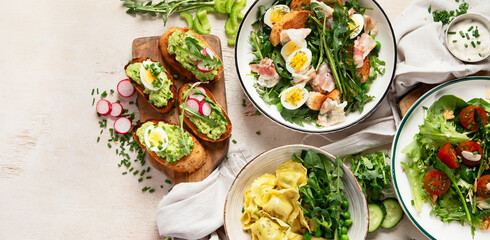 Spring fresh food with green leaf. Salads with strawberries, bacon and ravioli on light wooden background