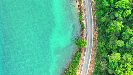 An epic drone view of a coastal asphalt road, meandering through lush, emerald landscapes, meeting...