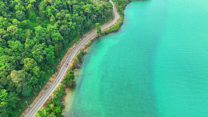 Aerial shot captures cars on a stunning tropical road, hugging the lush coastline, with vivid...