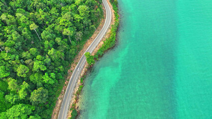 Cars traverse a mesmerizing asphalt road by the turquoise sea, embraced by lush, verdant landscapes from high above. Infrastructure and automobiles concept. Ko Chang, Thailand.  © Punyawee