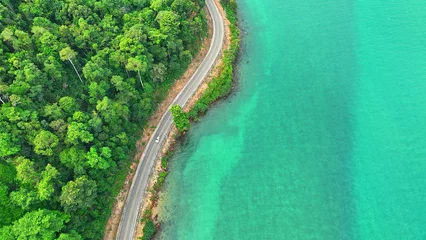 Fototapete Rund Cars traverse a mesmerizing asphalt road by the turquoise sea, embraced by lush, verdant landscapes from high above. Infrastructure and automobiles concept. Ko Chang, Thailand.  © Punyawee