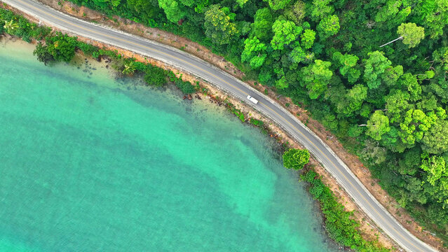 Aerial view captures cars cruising on a breathtaking coastal road beside turquoise seas, surrounded by lush greenery. Transportation and vehicles concept. Mu Ko Chang National Park, Thailand. 
