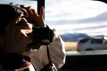A tourist person taking photo with a DSLR camera inside a car from road trip journey focusing on...
