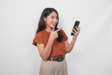 Happy Asian woman is smiling and pointing to her smartphone wearing brown shirt isolated by a white...