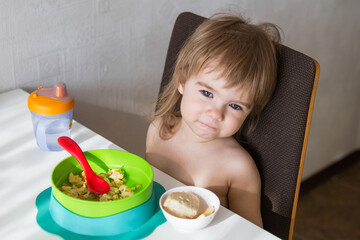 A joyful toddler girl sits in her high chair at home, eating scrambled eggs and toast for breakfast. Her face lights up with a big smile as she savors the delicious meal.