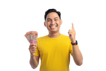 Smiling young Asian man holding money and pointing finger up with happy expression isolated on white background