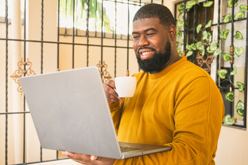 Black man relaxing at home in the morning with coffee enjoy using computer laptop addiction to...
