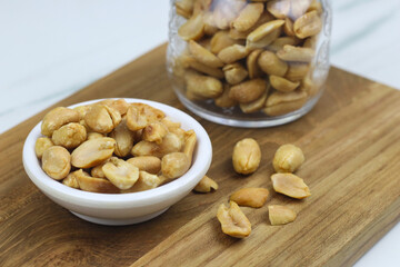 Kacang goreng or fried peanuts in a jar and white plate. Indonesian snack with marble white background, selective focus.