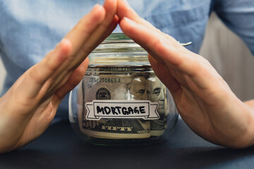 Female hands holding Glass jar full of American currency dollars cash banknote with text MORTGAGE....