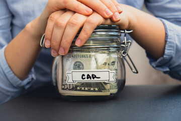Unrecognizable woman holding Saving Money In Glass Jar filled with Dollars banknotes. CAR transcription in front of jar. Managing personal finances extra income for future insecurity background