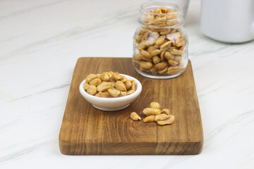 Kacang goreng or fried peanuts in a jar and white plate. Indonesian snack with marble white background, selective focus.