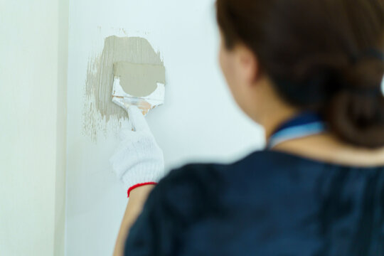 Happy woman using painting brush paints the empty white wall during home renovation.