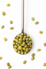 Dry, green mung beans in iron spoon on white background