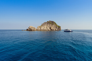 Fototapeta na wymiar Tranquil sea surrounds a boat by a picturesque rocky island under a clear blue sky at Chumporn, Thailand