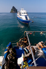 Scuba divers gearing up on a boat with clear blue water and tropical island in the background