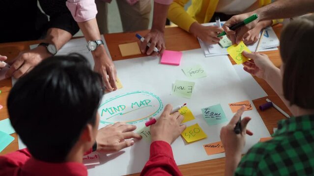 Top view of business team in casual cloth hand writing idea on sticky notes. Closeup of diverse people brainstorming marketing idea while sticking colorful sticky notes on mind mapping. Convocation.