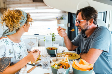 A happy couple spending time together having fun during lunch inside a camper. People with campers smiling thinking about the new destination. Man and woman eating peacefully