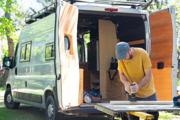 Man sanding wood with an electric sander customizing a camper van - obrazy, fototapety, plakaty
