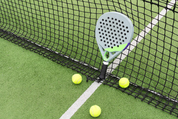 Yellow balls on grass turf near padel tennis racket behind net in green court outdoors with natural lighting. Paddle is a racquet game. Professional sport concept with copy space.
