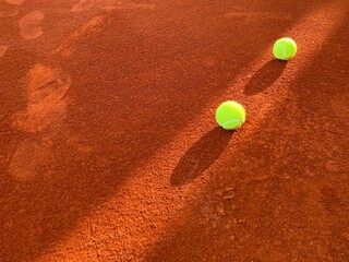 A beam of light passed through two green tennis balls on the orange clay tennis court