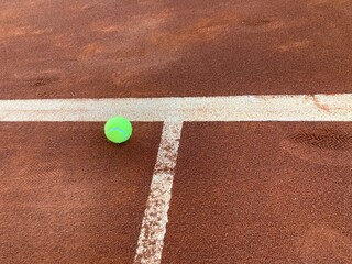the bright green tennis ball lands exactly on the center line of the red clay court