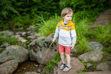 Cute little boy with a backpack having fun outdoors on sunny summer day. Child exploring nature. Kid going on a trip.