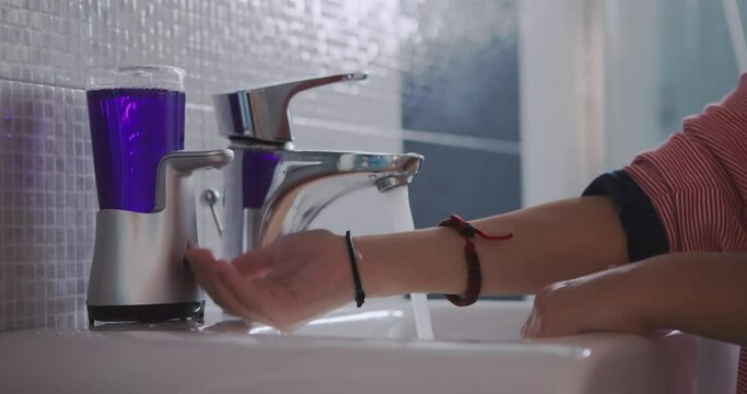 A young boy standing on a stool to reach the sink is diligently washing his hands with soap and water in a clean bathroom.