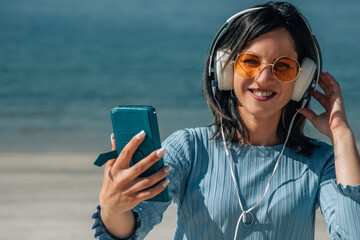 woman with headphones and mobile phone listening to music on the beach