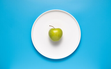 Fresh green apple on a white plate on a blue background