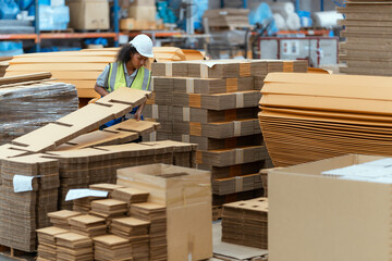 Machine operators work in a large paper factory and check stock of cardboard boxes.