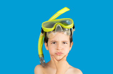 Pensive kid with snorkel mask tuba and snorkel looking at camera thinking isolated on a blue background,Hand on chin thinking about question, pensive expression .Snorkeling, swimming, vacation concept