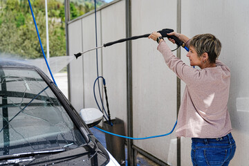 Intense concentration as woman uses high-pressure water on car.