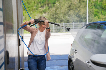 Woman in a power stance cleaning her car with a high-pressure hose.