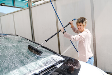 A focused woman scrubs her car with a high-pressure water brush.