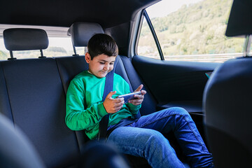 Child focused on smartphone, oblivious to scenic drive.