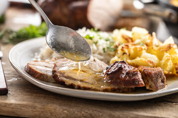 A close-up view of a spoon with sauce that pours over the meat, roasted neck. As a side dish to the meat are baked potatoes and jasmine rice - 794920290