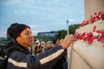 Man placing red poppies on the wall at the Court of Honour. Unrecognizable people in uniform in the background. Anzac Day commemoration. Auckland Domain. - obrazy, fototapety, plakaty